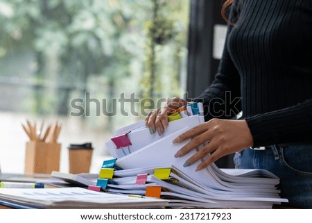 secretary searches through stacked documents on desk in office to find lease within stacked documents just before meeting. concept difficulty in finding hire purchase contract from stacked documents