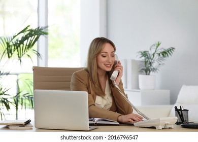 Secretary talking on phone at wooden table in office - Shutterstock ID 2016796547