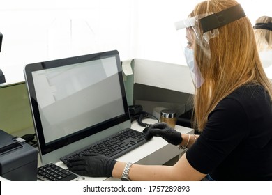 Secretary Works On The Computer Protected By A Visor, Surgical Mask And Plexiglass Screen