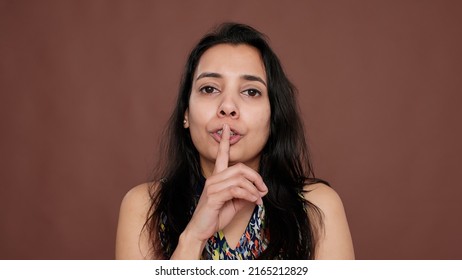 Secretive adult keeping secret with mute and silence sign, holding finger over mouth. Confidential private information doing hush gesture, not sharing unbelievable rumor and gossip.