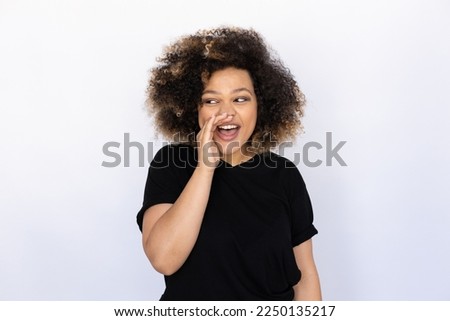 Secretive woman telling secret. Young female model holding hand at mouth, looking aside and talking. Portrait, studio shot, secrecy concept