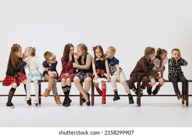 Secrets. Cute, funny children, little girls and boys sitting on banch isolated on grey studio background. Beauty, kids fashion, education, happy childhood concept. Copy space for ad.