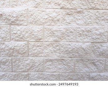 A section of a beige brick wall with a clean, smooth concrete sidewalk in the foreground. The wall textured surface and uniform brick pattern provide a neutral backdrop, while the sidewalk adds a