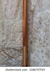   Section Of A Copper Pipe Located Vertically On A White Stone Wall                                 