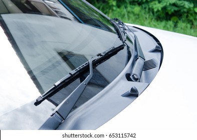 Section of the front of a white vehicle and its front windscreen bonnet and wipers.