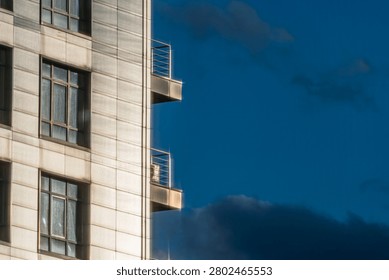 Section of modern building featuring architectural details, light-colored concrete panels, windows, balconies, deep blue sky, clear day lighting, urban scene