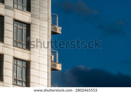 Section of modern building featuring architectural details, light-colored concrete panels, windows, balconies, deep blue sky, clear day lighting, urban scene