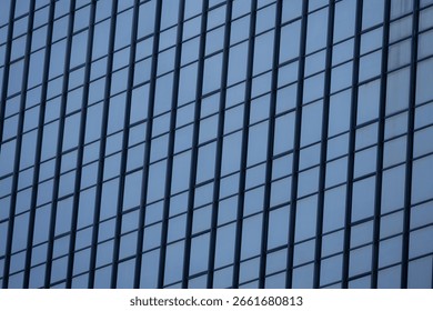 A section of a modern building with many rectangular glass windows reflecting the clear, bright blue sky.