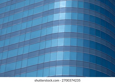 A section of a modern building with many rectangular glass windows reflecting the clear, bright blue sky.