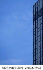 A section of a modern building with many rectangular glass windows reflecting the clear, bright blue sky.