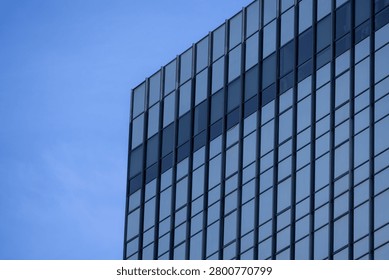 A section of a modern building with many rectangular glass windows reflecting the clear, bright blue sky.