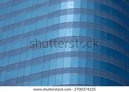 A section of a modern building with many rectangular glass windows reflecting the clear, bright blue sky.