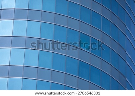 A section of a modern building with many rectangular glass windows reflecting the clear, bright blue sky.