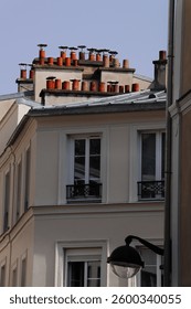 A section of a multi-story building, showcasing its architectural features and the unique rooftop details with many chimney pots with a foreground street lamp 