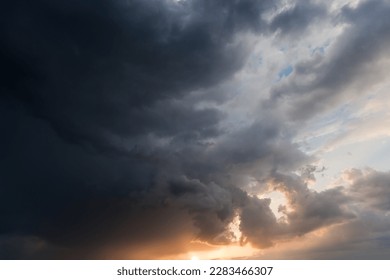 Section of the sky with part of the dense dark storm cloud at sunset in summer 