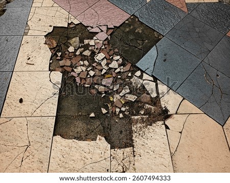 A section of tiled pavement is severely damaged, with cracked and missing tiles revealing dirt and broken fragments beneath. The remaining tiles show wear and discoloration.