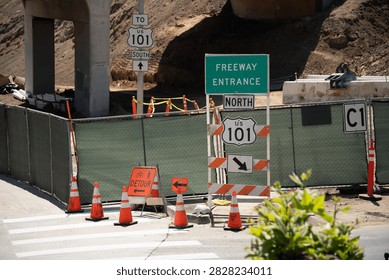 A section of US Highway 101 is undergoing construction, indicated by detour signs, orange traffic cones, and temporary fencing