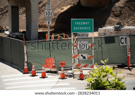 A section of US Highway 101 is undergoing construction, indicated by detour signs, orange traffic cones, and temporary fencing