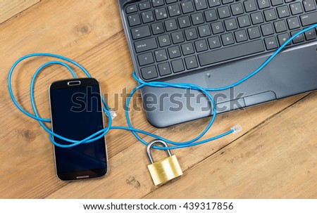 Secure internet system: Smart phone and computer keyboard connected with safety lock and blue wire.
Overhead view with electronic devices on wooden office desk.