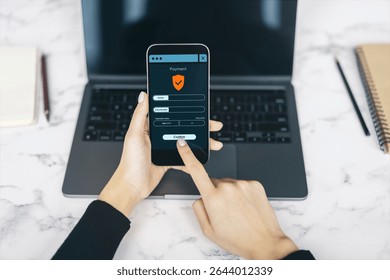 Secure mobile payment interface on smartphone held by user with laptop and notebooks on marble desk background, illustrating digital transaction
