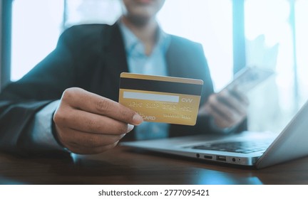 Secure online payment e-commerce financial transaction concept business person holding credit card and smartphone purchasing goods via laptop computer at modern office