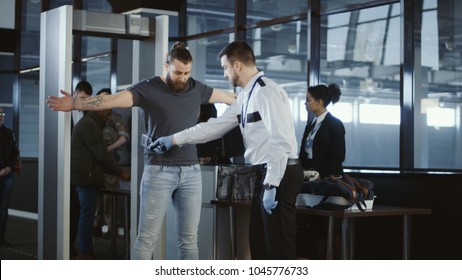 Security agent at an airport check-in gate patting down a bearded casual male passenger with outstretched arms after he passes through the metal detector scanner in the departures hall. - Shutterstock ID 1045776733