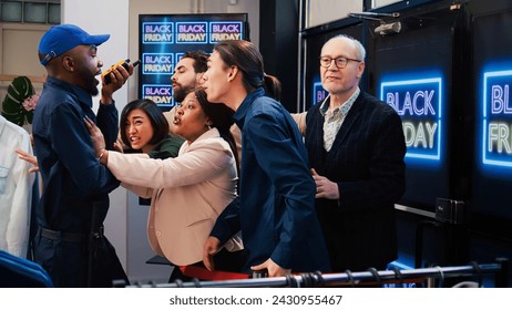 Security agent hold back eager clients acting aggressive on black friday promotional launch, diverse people lined up at store entrance. Anxious violent customers pushing red tape line, screaming.