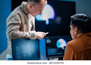 A security analyst explains on-screen data to a seated teammate in a shadowy data monitoring room lit by screen glow. The frame illustrates protecting critical data.