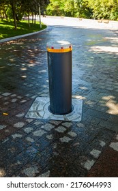 Security Bollard To Block Or Enable Traffic. Bollard With Warning Light For Physical And Visual Barrier. Black Steel Bollard For Road Traffic Control. Metallic Bollard With Orange Safety Reflector