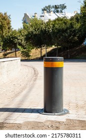 Security Bollard To Enable Or Block Traffic. Bollard With Warning Light For Physical And Visual Barrier. Black Steel Bollard For Road Traffic Control. Metallic Bollard With Orange Safety Reflector