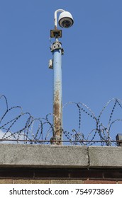 Security camera behind a barbed wire topped brick wall