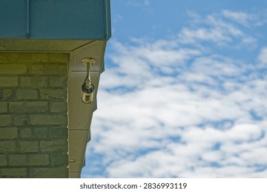 A security camera is installed on the corner of a brick building with a blue roof against a bright sky filled with scattered clouds.