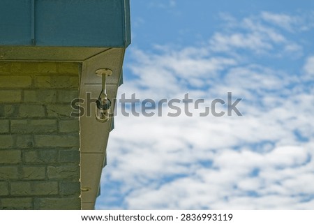 A security camera is installed on the corner of a brick building with a blue roof against a bright sky filled with scattered clouds.