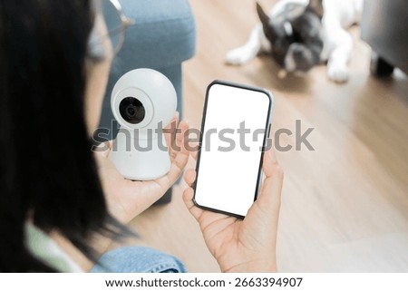 Security camera. IP Camera with phone on women hand holding while relaxing at home with her dog. Pet care concept.