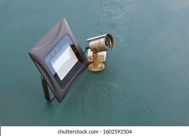 A Security Camera With Motion Detection LED Floodlights Installed On A Wall Outside A House To Deter Theft, Robbery Or Break-ins. CCTV System With LED Spotlight Setup To Provide Security For A Home.