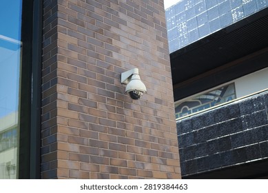 A security camera is mounted on a brick wall in a city setting.