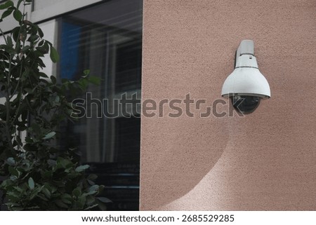 Security camera mounted on building wall near greenery