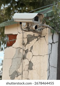 Security camera mounted on cracked building wall showing urban decay and infrastructure. Mobile photo