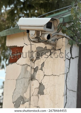 Security camera mounted on cracked building wall showing urban decay and infrastructure. Mobile photo