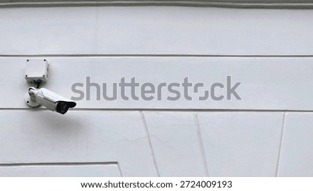 security camera on the wall.CCTV.A security camera is mounted on a plain white wall.A security camera is fixed on a plain white wall. The camera is positioned to monitor the area outside, likely during daytime, ensuring safety and security.