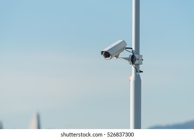 Security camera pointing to down on a pole on a blue sky background