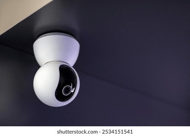 A security camera is positioned and securely hanging from the ceiling in a dark and dimly lit room, monitoring the surroundings continuously