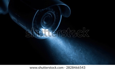 A security camera with a visible blue light beam, captured in a dark, atmospheric setting.