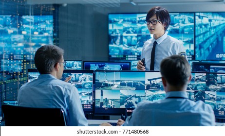 In The Security Control Room Chief Surveillance Officer Briefs Two Of His Subordinates. Multiple Screens Show That They Guard Object Of Big Importance.