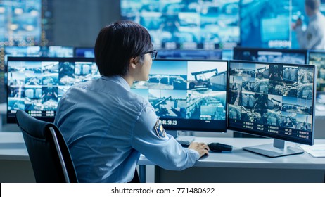 In The Security Control Room Officer Monitors Multiple Screens For Suspicious Activities. He's Surrounded By Monitors And Guards Facility Of National Importance.