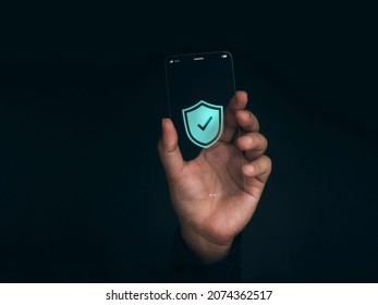 Security data technology and personal privacy on future phone concept. Shield with checkmark icon on the thin screen of futuristic transparent super slim glass smartphone in hand on dark background.