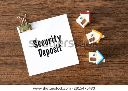 Security Deposit text on white paper with toy houses and binder clips on wooden desk, real estate rental concept