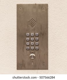 Security. Found On The Outside Of Gated Communities, A Voice Door Entry Phone With Key Pad For Codes To Be Entered Found On A Concrete Cream Stucco Wall. 