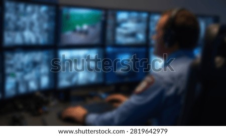 A security guard intently watches multiple CCTV camera feeds displayed on a bank of monitors in a dimly lit control room.