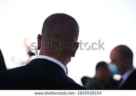 Security guard listening to his earpiece on event. Back of jacket showing. secret service guard. private bodyguard. man with earpiece in crowd. Black suit.